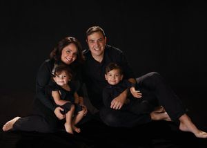 Family of four in matching black outfits posing together on dark background in professional studio portrait.