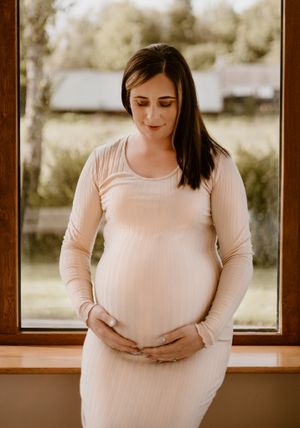 maternity photoshoot near a window in a cream dress