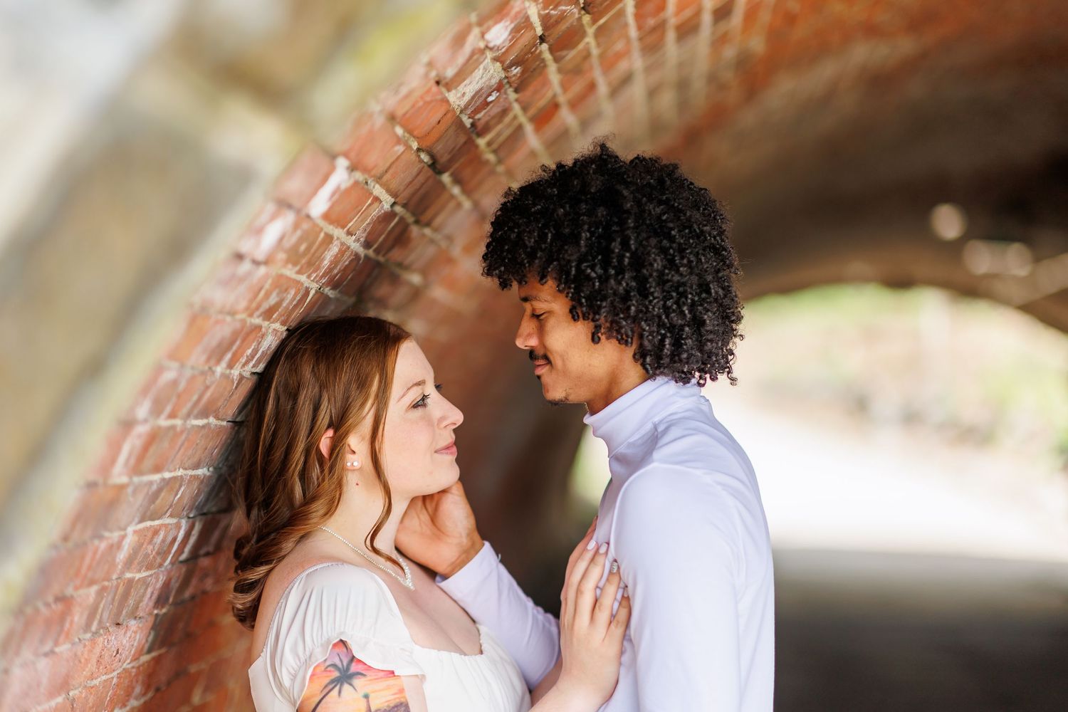 Romantic couples photoshoot under a brick archway in soft natural lighting.