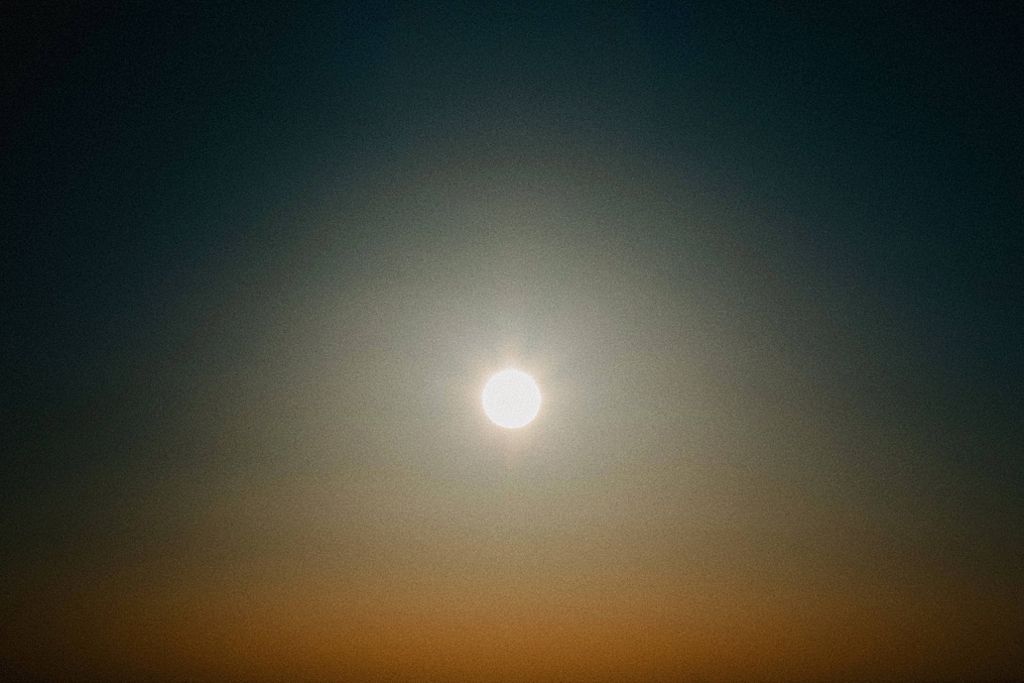 Glowing sun in a dark sky creates a hazy atmospheric effect at dusk.