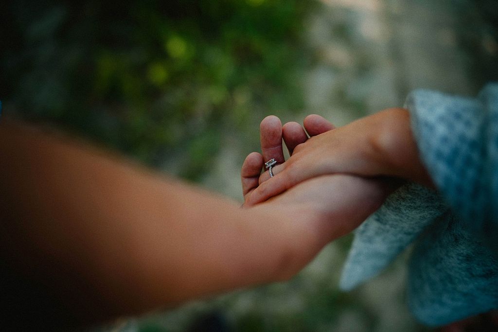 Close up of hands holding engagement ring in soft natural lighting.