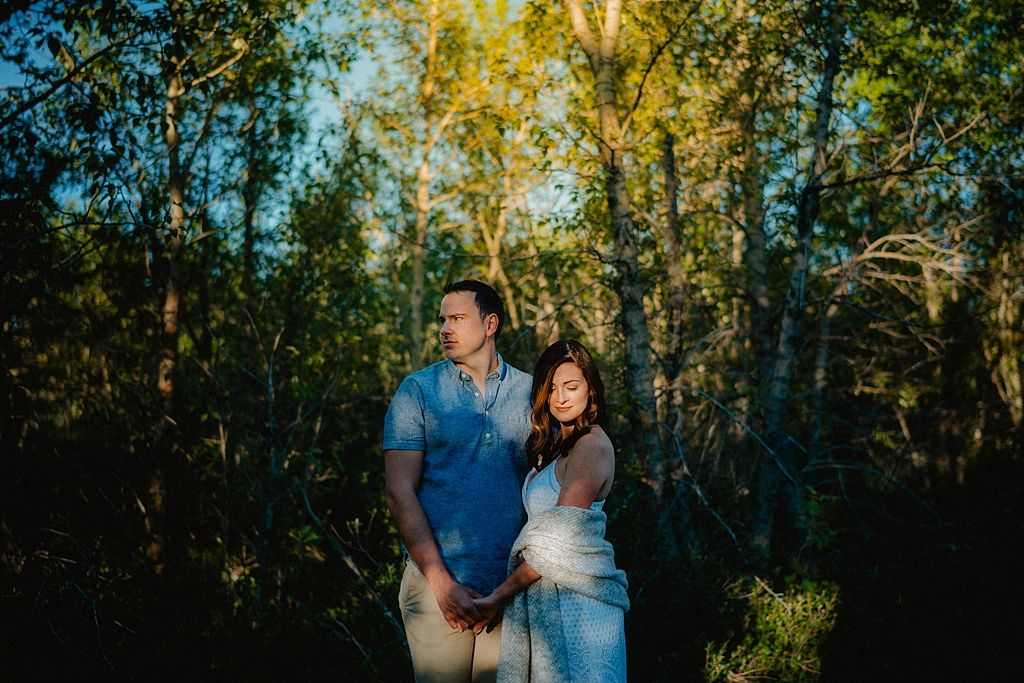 Couple in casual attire walking through sunlit forest with golden leaves.