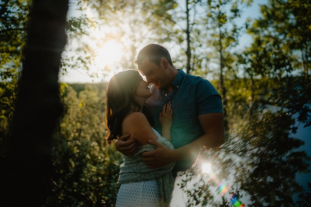 Couple sharing intimate moment in sunlit forest clearing with lens flare effect.