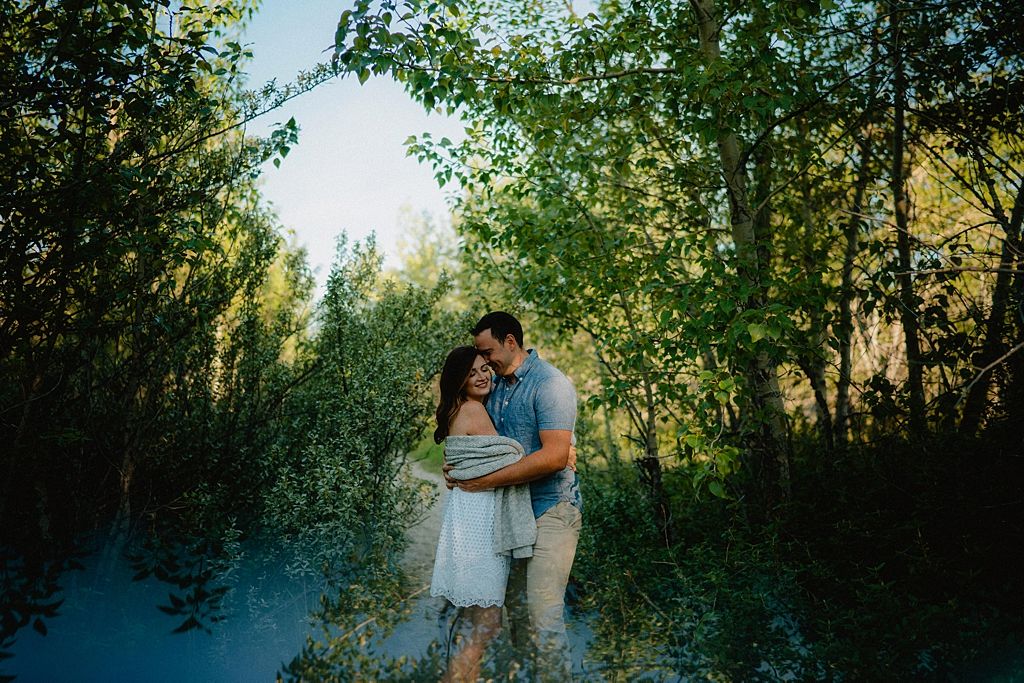 Two people share an intimate moment on a wooded path with sunlight filtering through trees.