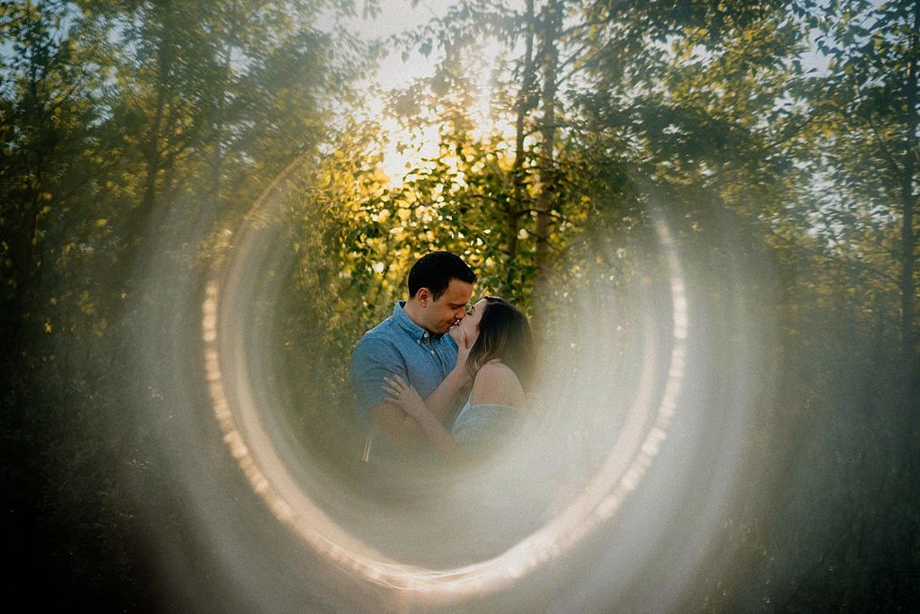 Dreamy circular lens effect captures a couple's tender moment in a sunlit forest setting.