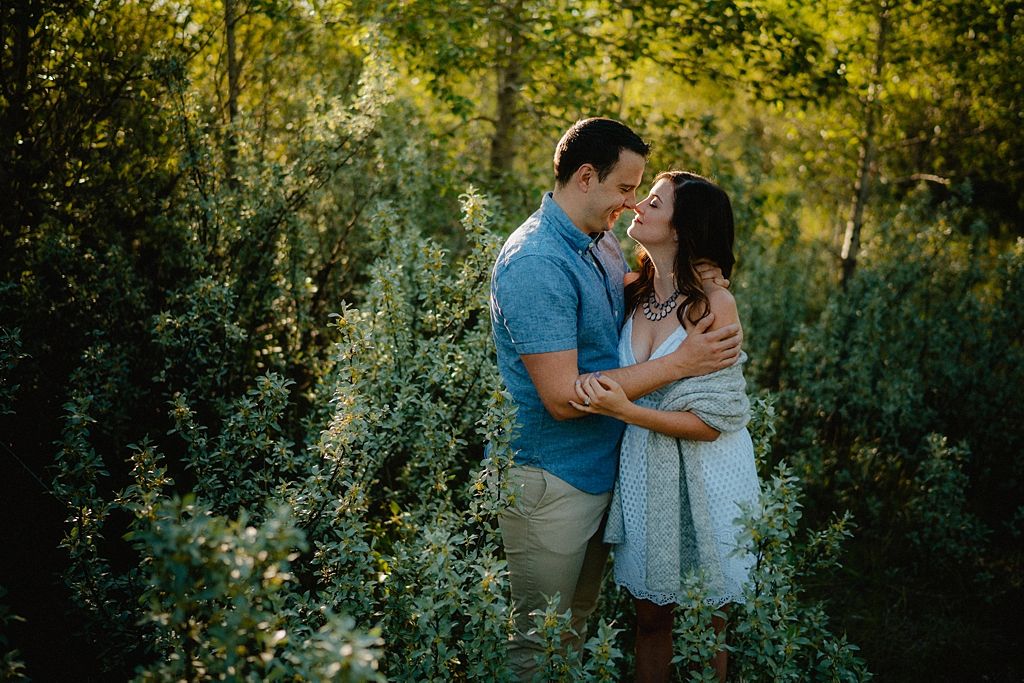 An affectionate couple shares intimate moments in a sunlit forest clearing.