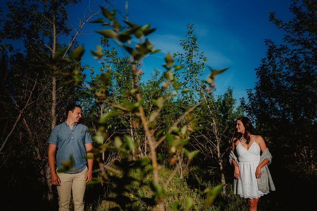 A couple poses against a deep blue sky surrounded by green foliage at dusk.