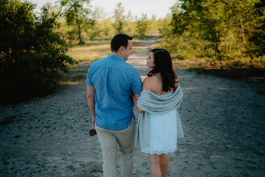 Two people walking together on a sandy path surrounded by natural vegetation.