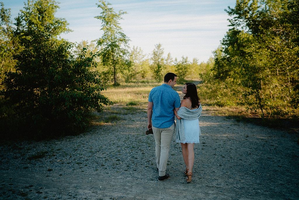A couple strolls together on a sandy trail through green woodland scenery.