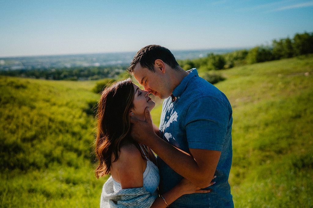 Romantic moment captured against rolling green hills and blue sky backdrop.