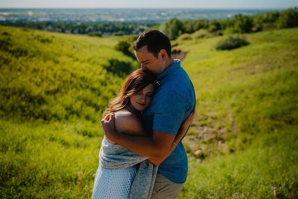 Couple embracing on a hilltop overlooking a scenic valley under blue skies.