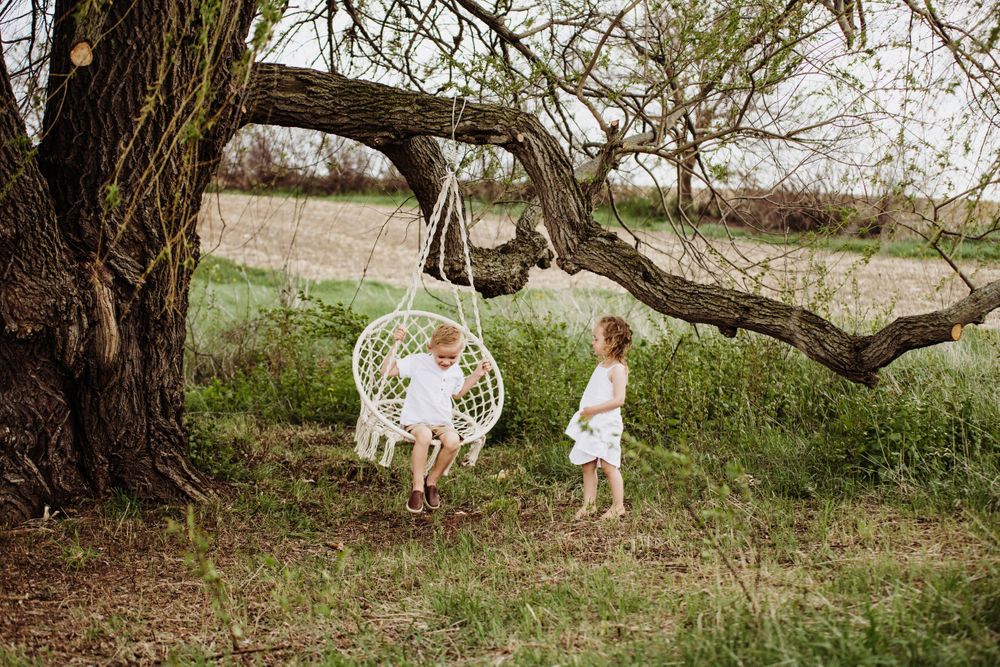 Natural outdoor family photoshoot featuring a rattan hanging chair under a large tree.