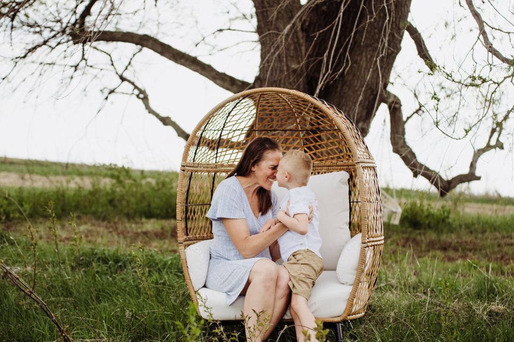 Hanging rattan chair with plush white cushions nestled under a tree branch.