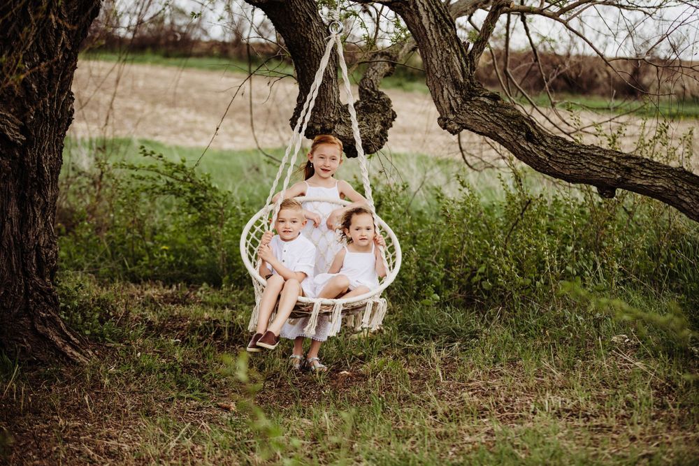 Siblings and family members gathered around a woven hanging chair in a peaceful outdoor garden setting.