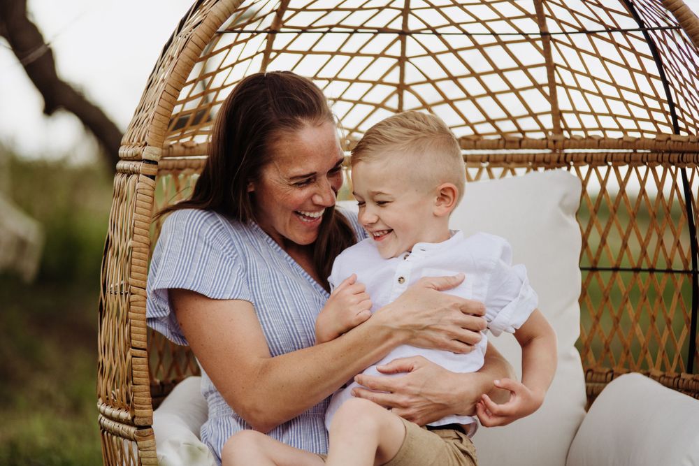 Joyful interaction in a hanging rattan chair set against a natural backdrop.
