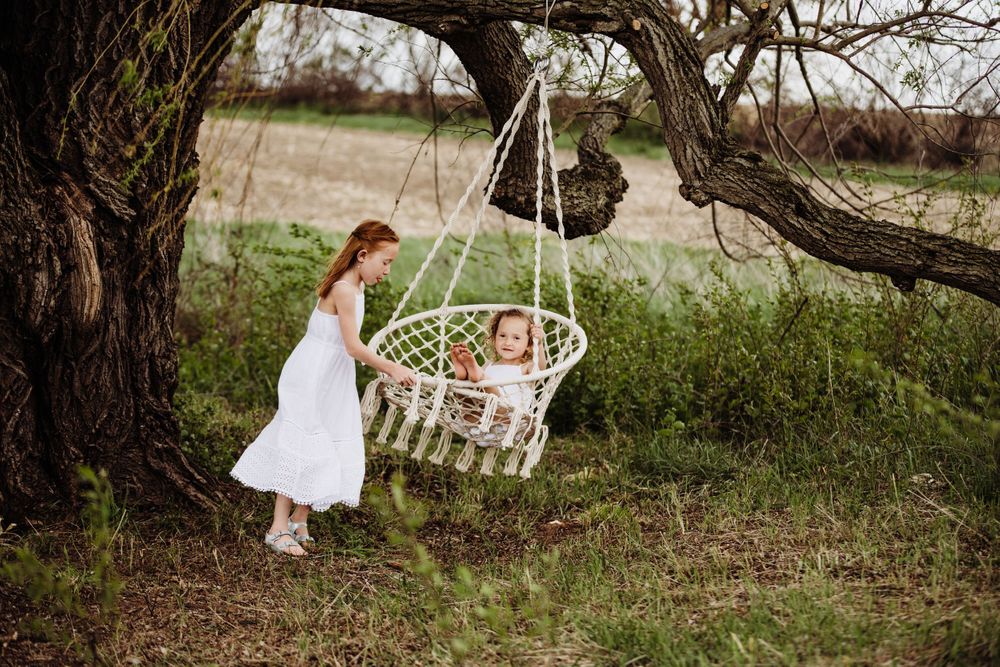 Rustic outdoor scene with hanging rattan chair against natural landscape background.