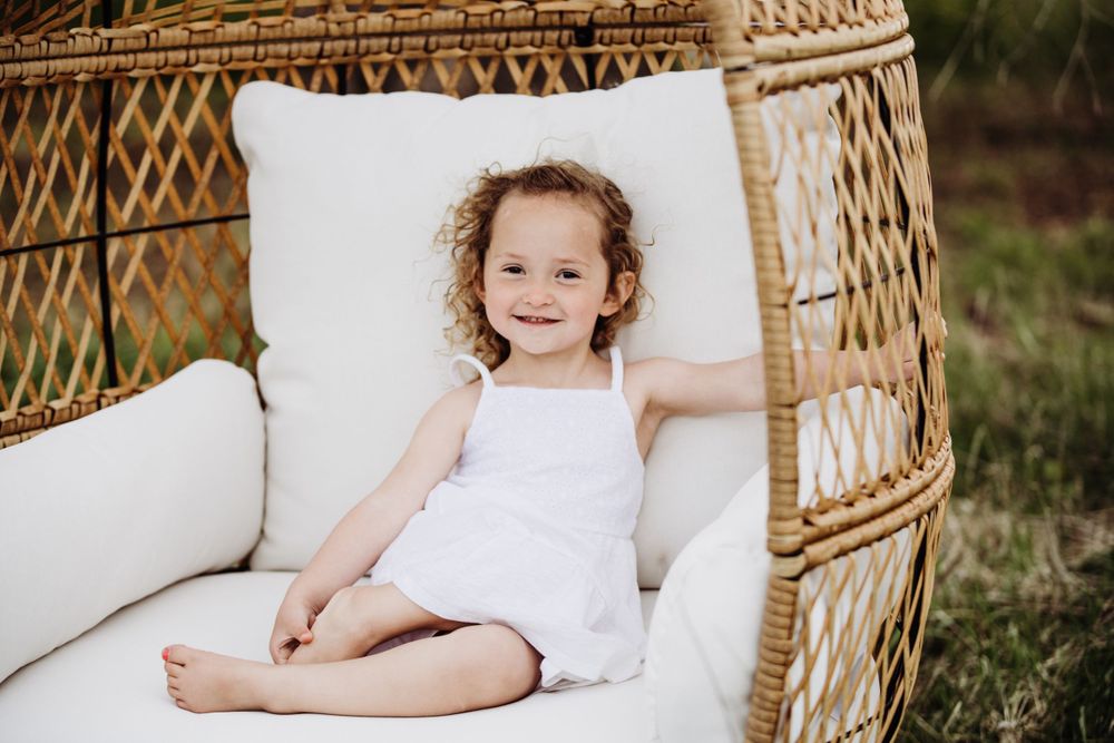 Cozy woven hanging chair with white cushions photographed in outdoor garden setting.