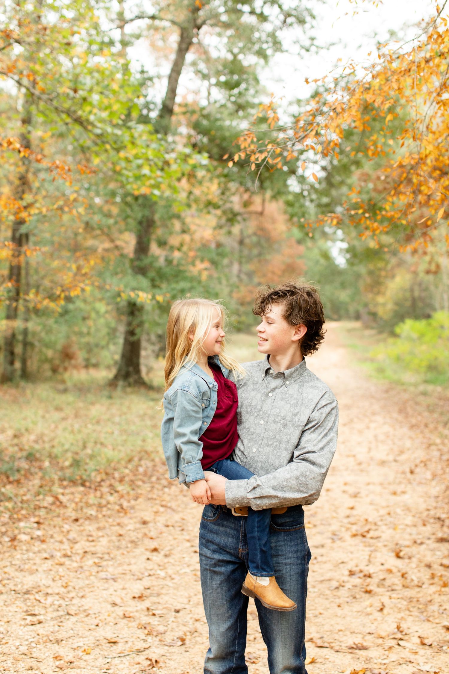 Candid moment between loved ones on a leaf-covered forest path in fall.