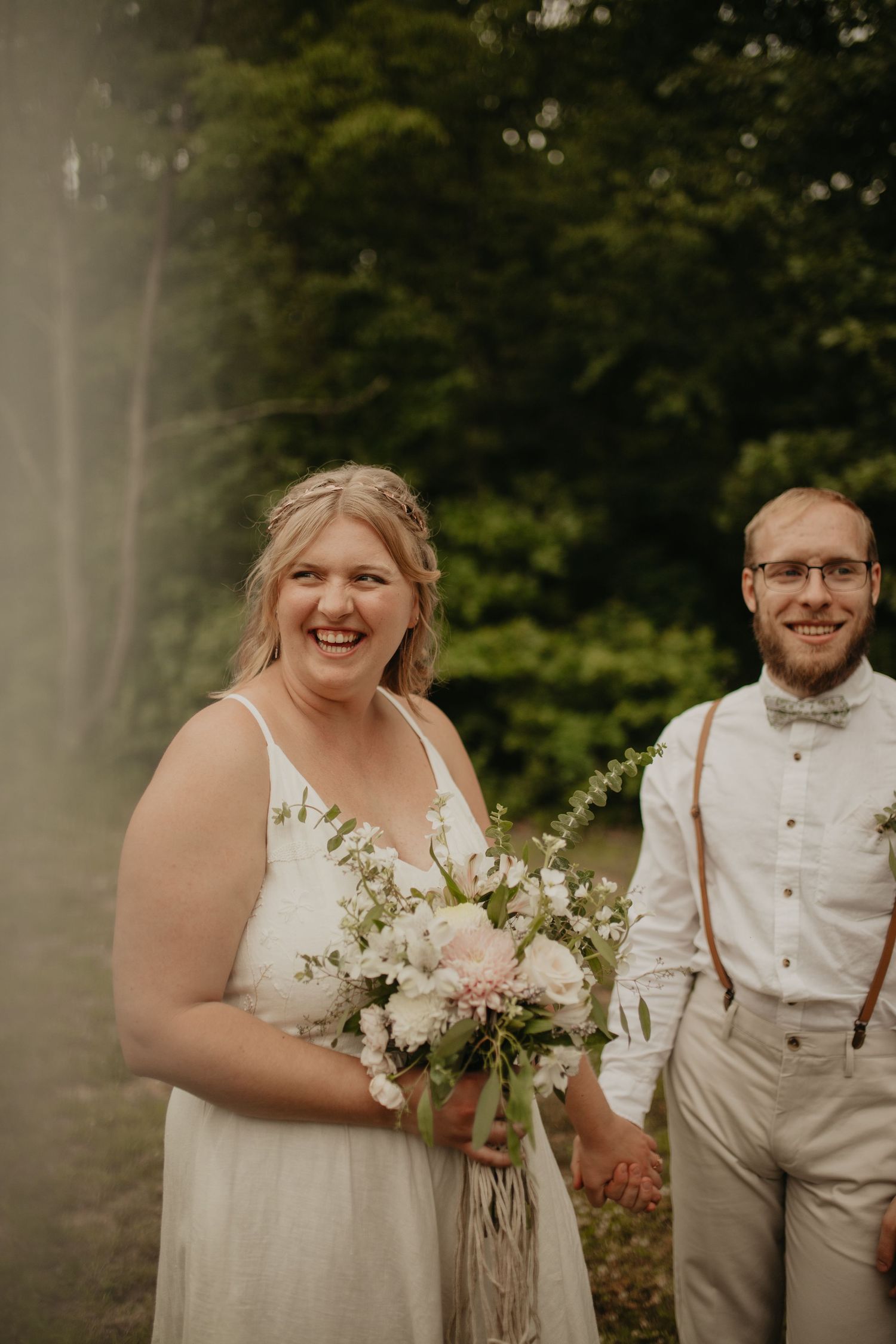 Newlyweds share joyful moment in garden setting with white floral bouquet.