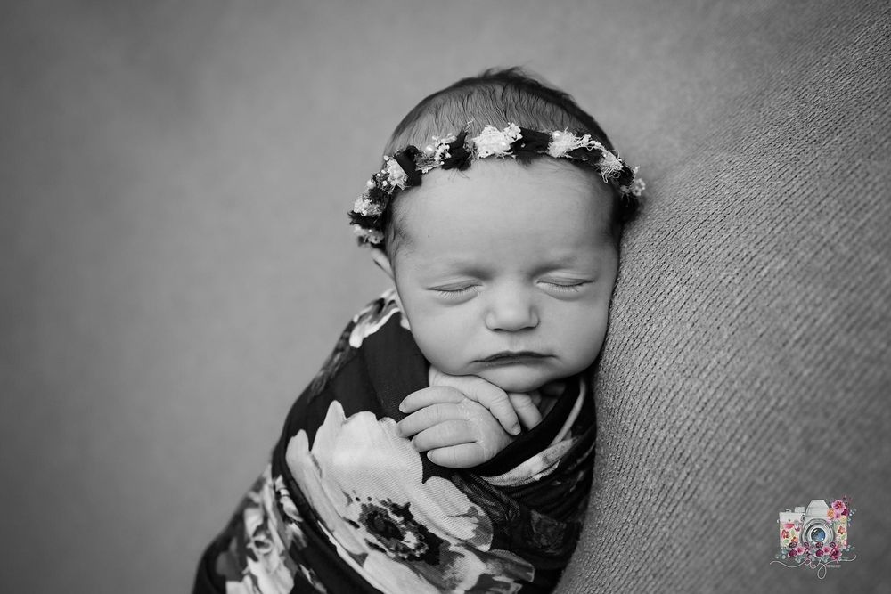 Black and white portrait of sleeping newborn wearing floral crown and wrap.