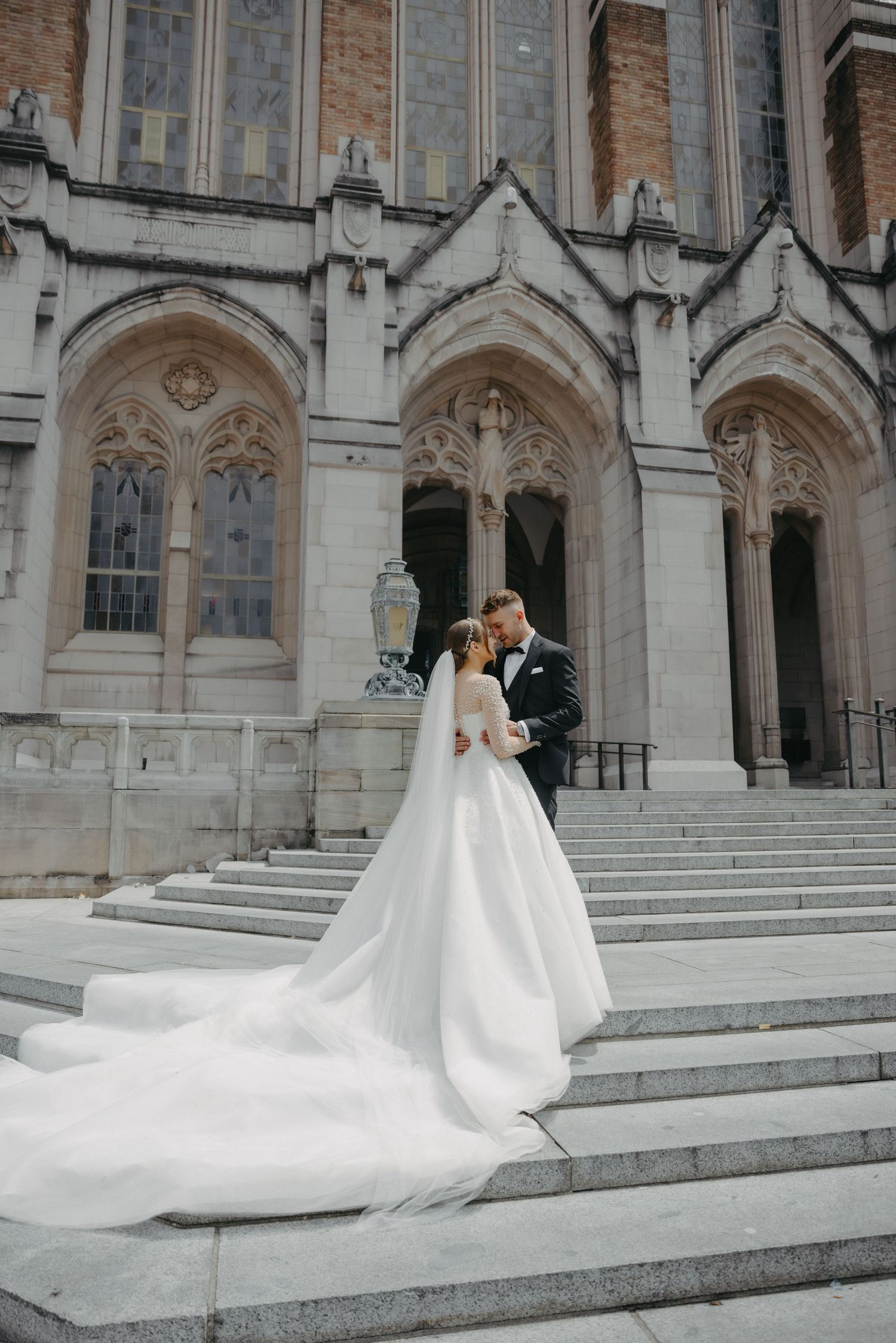 Newlyweds share romantic moment on church steps with dramatic cathedral architecture.