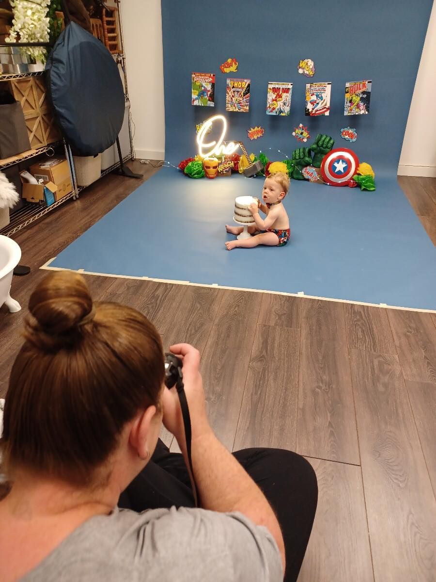 Behind-the-scenes newborn photography setup with superhero themed backdrop and props.