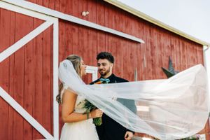 Wind catches bridal veil during portrait session in front of red barn.