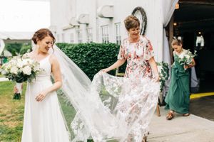 A bride and wedding party members carrying dresses while walking outside.