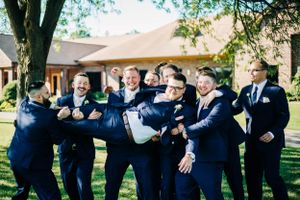 Groomsmen in navy suits pose playfully on a sunny lawn.