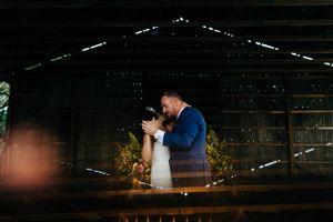 Newlyweds share an intimate moment in a dimly lit rustic barn setting.