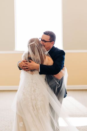 A tender embrace between newlyweds with flowing veil in a bright room.