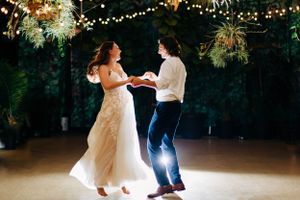 A romantic first dance at a wedding reception under twinkling lights and greenery decorations.
