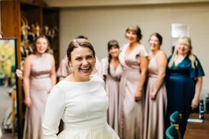 Wedding party members in blush and neutral dresses share a joyful moment while getting ready.