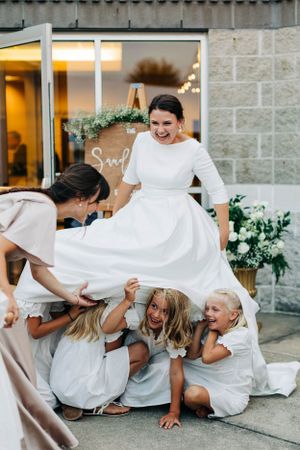 Playful moment with children peeking under a wedding dress on the sidewalk.