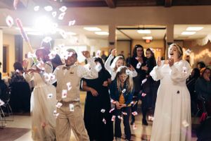 Wedding guests dance and celebrate during a reception with floating confetti and bright lights.