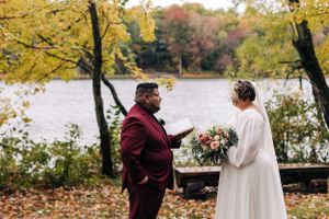 Autumn wedding ceremony by lake with golden foliage in background.