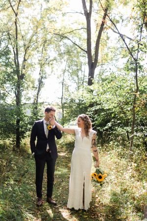 A tender moment between a couple in formal attire surrounded by sunlit forest greenery.