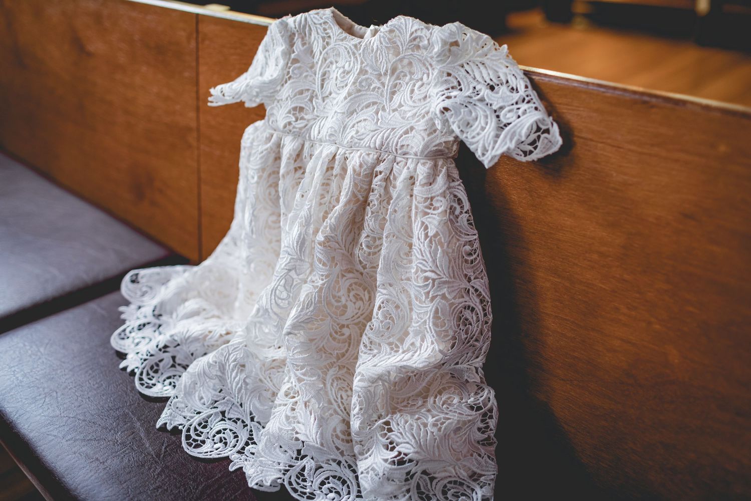 Delicate white lace christening dress displayed on dark surface.