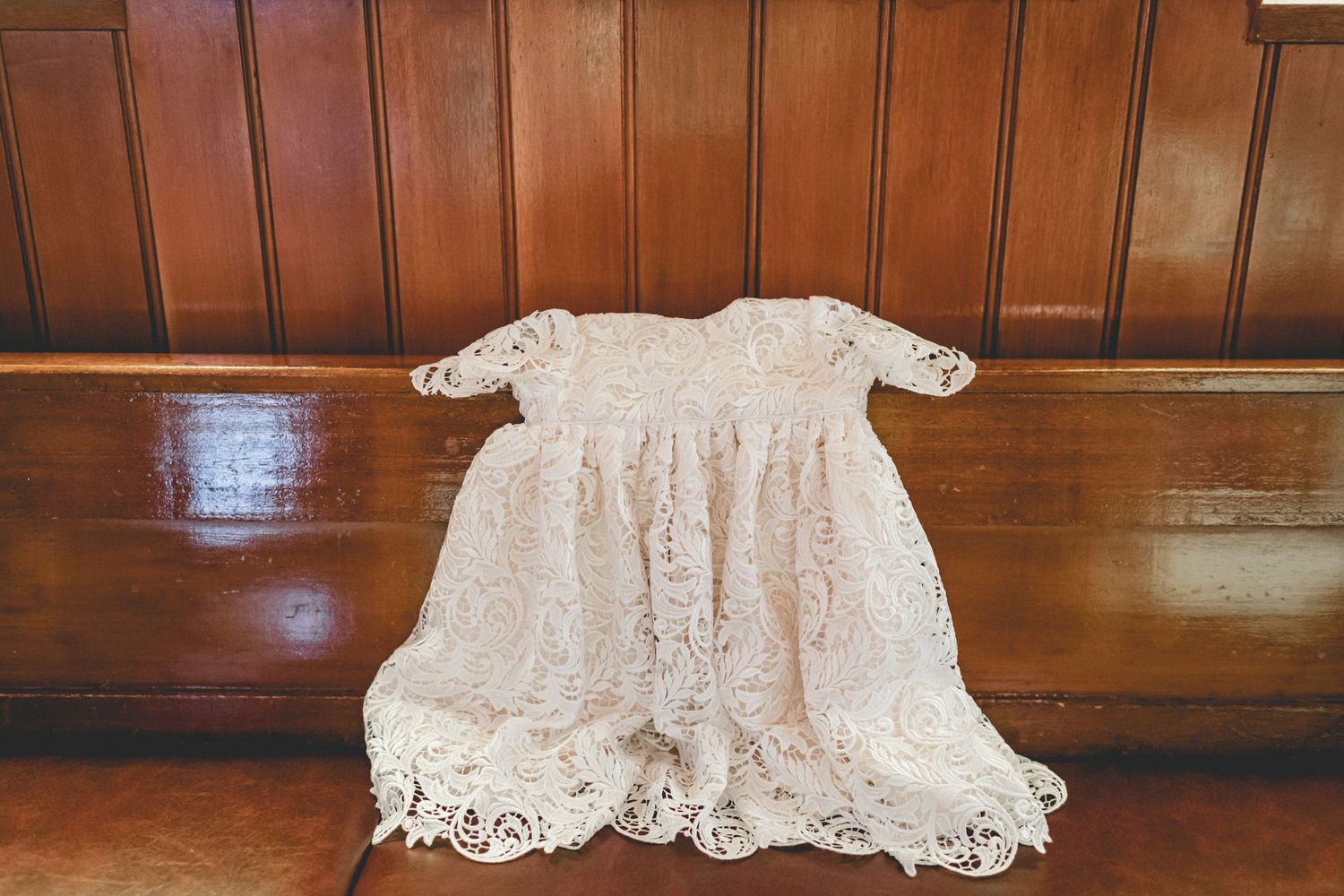 Vintage white lace christening gown displayed on wooden bench.