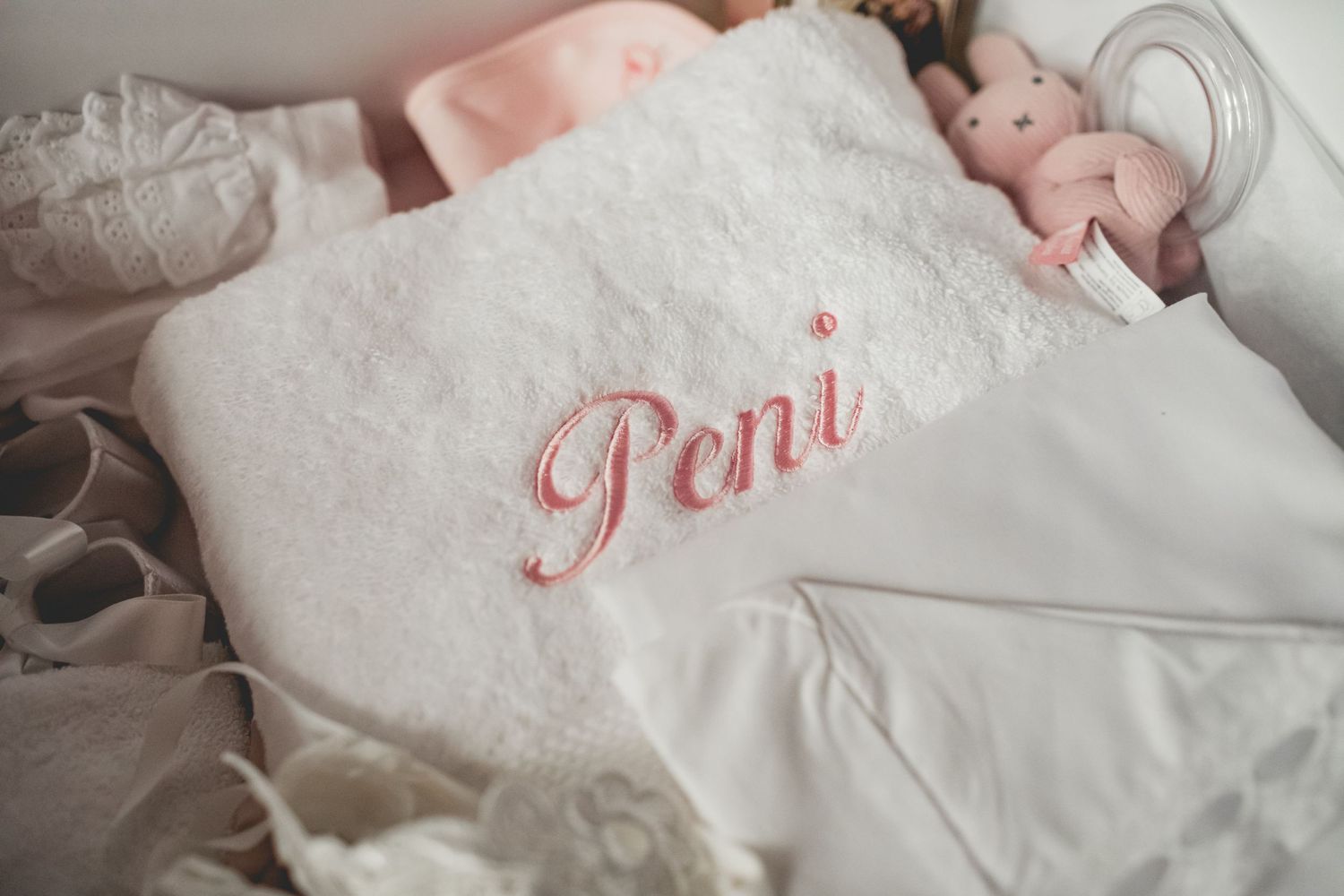 White blanket with pink embroidered 'Poni' text against soft background.