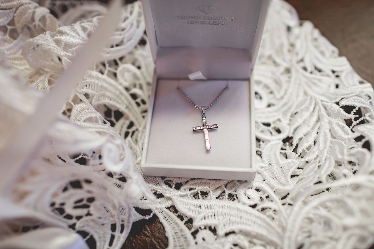 Silver cross necklace in white jewelry box on lace fabric.