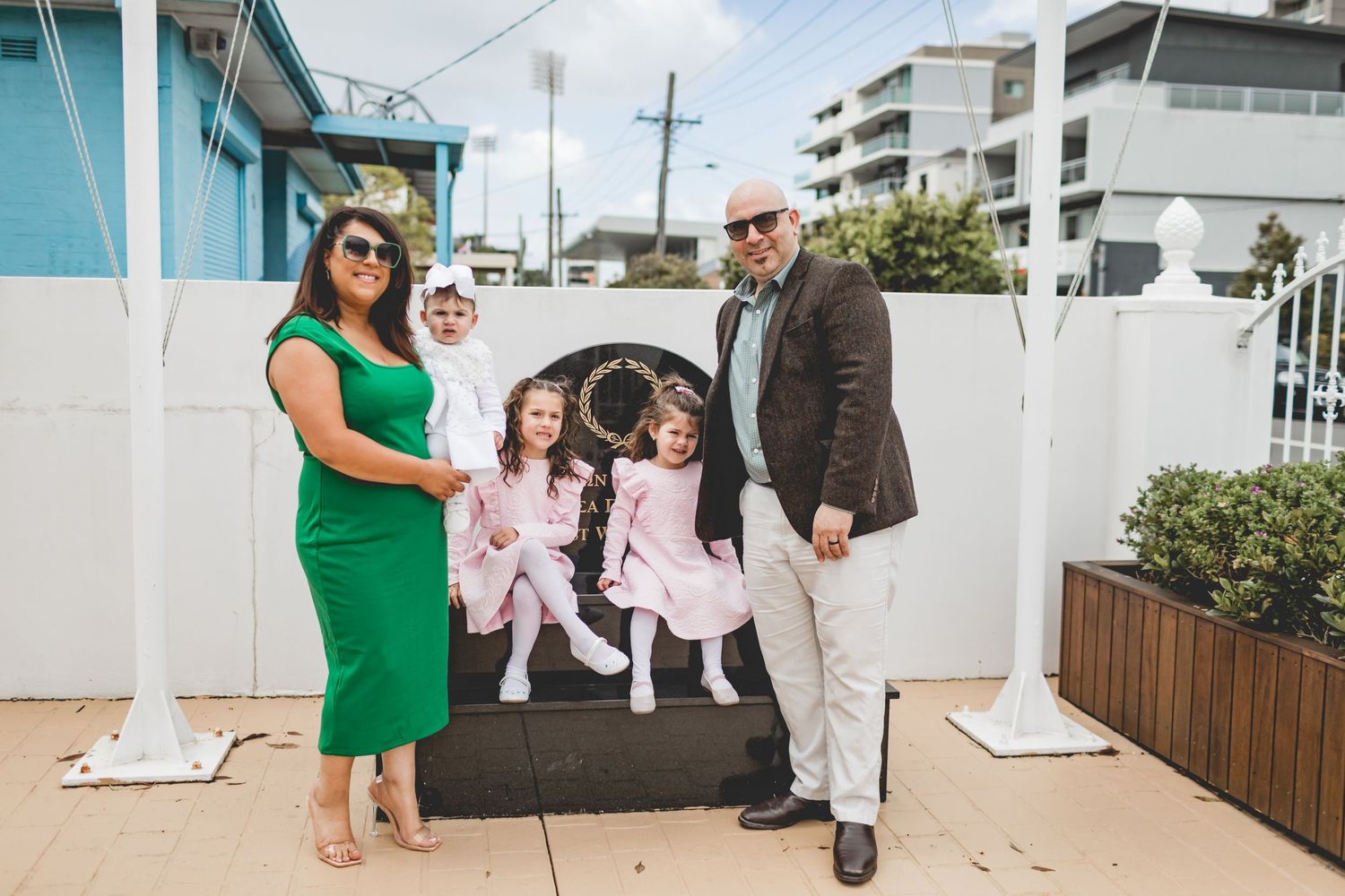 Family portrait on an outdoor patio with turquoise building in background.