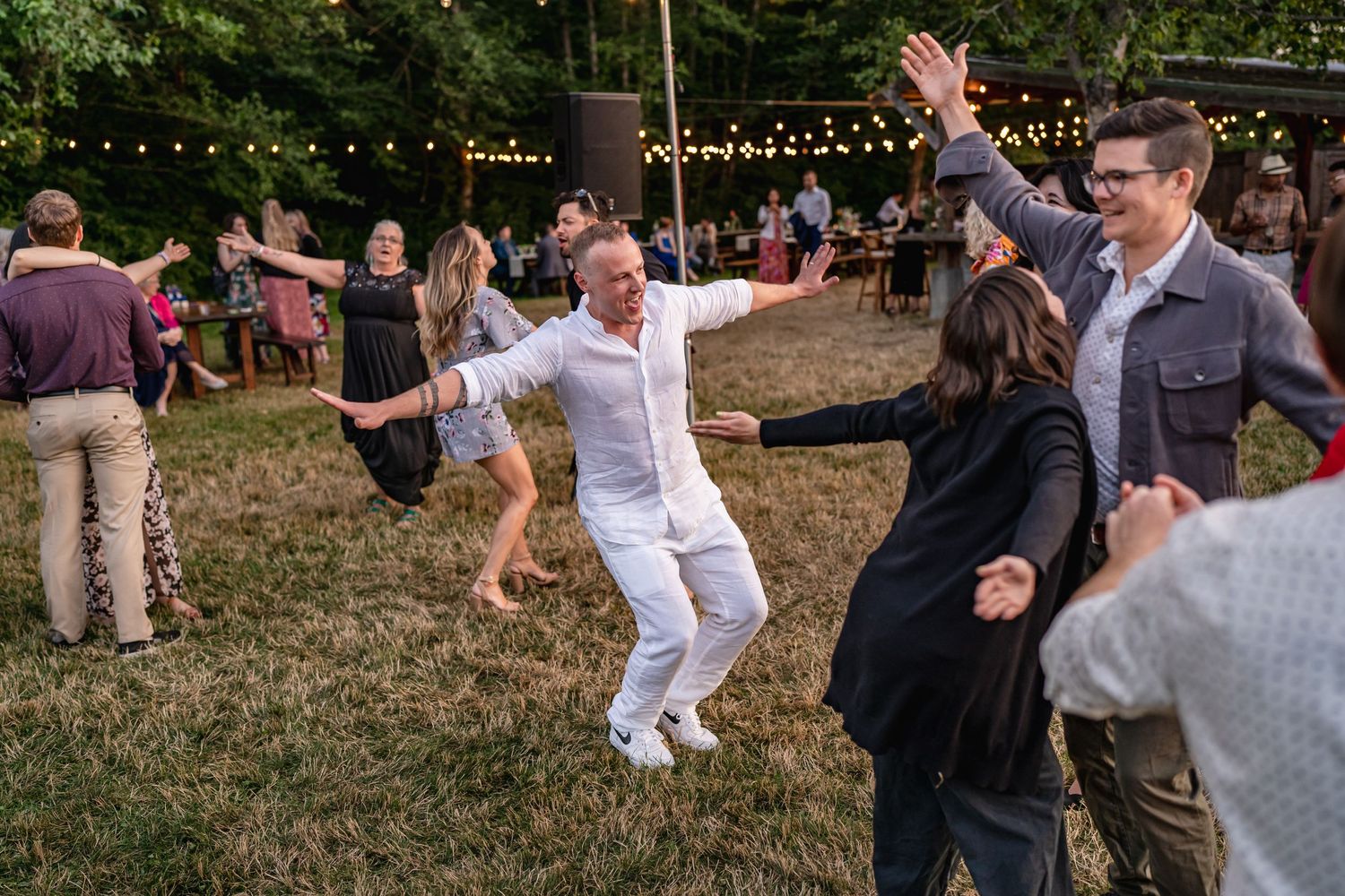 Guests dancing and celebrating at outdoor wedding reception with string lights overhead.