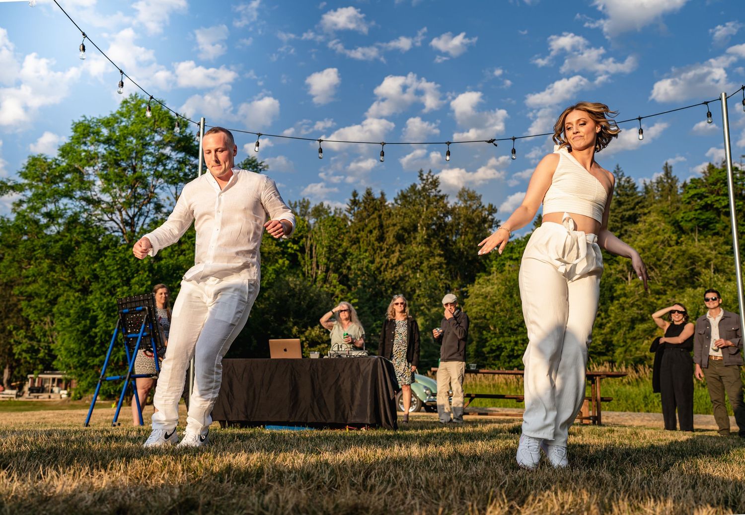 Wedding couple jumping joyfully during outdoor reception celebration.