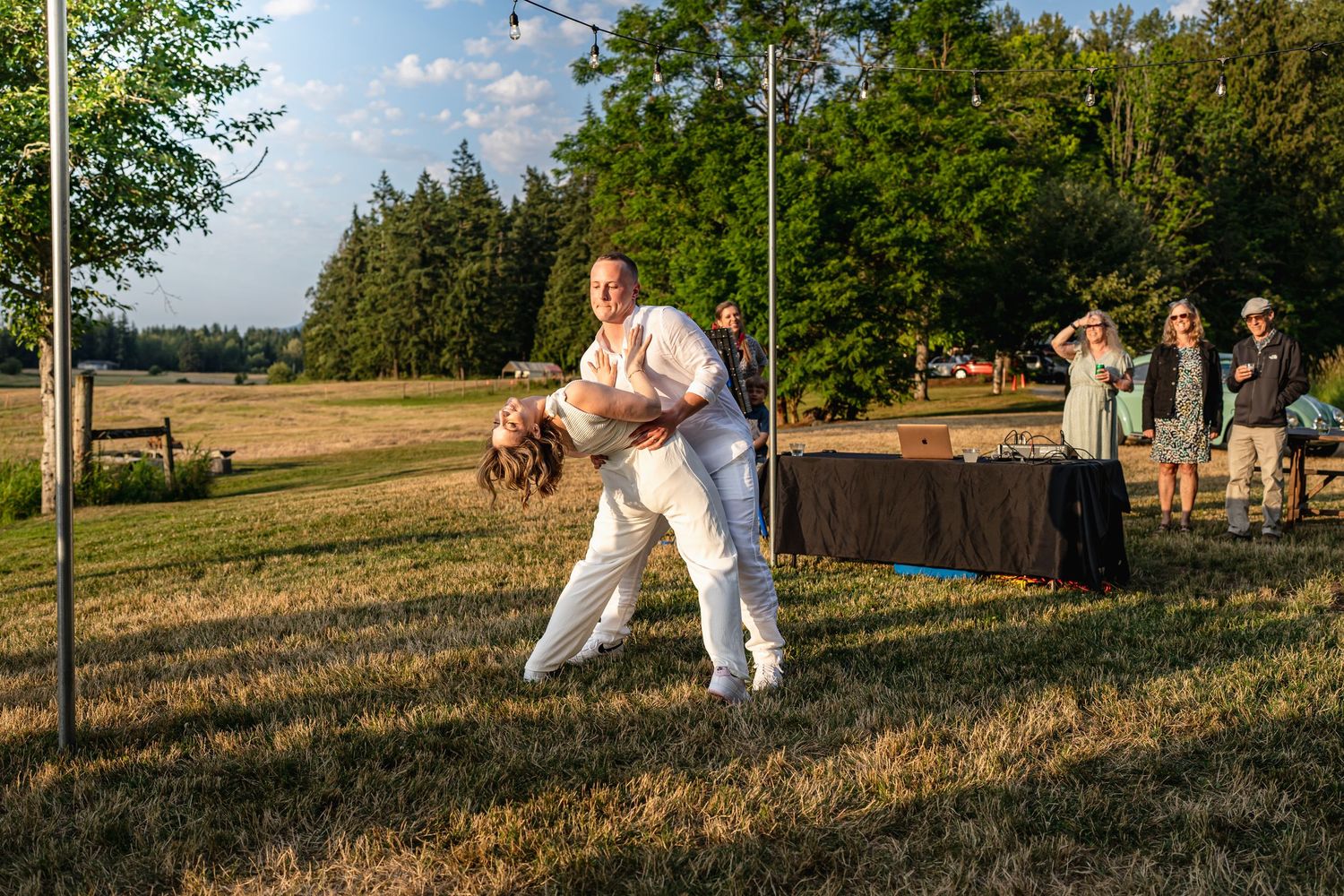 A couple performs a dip dance move during an outdoor wedding at sunset.