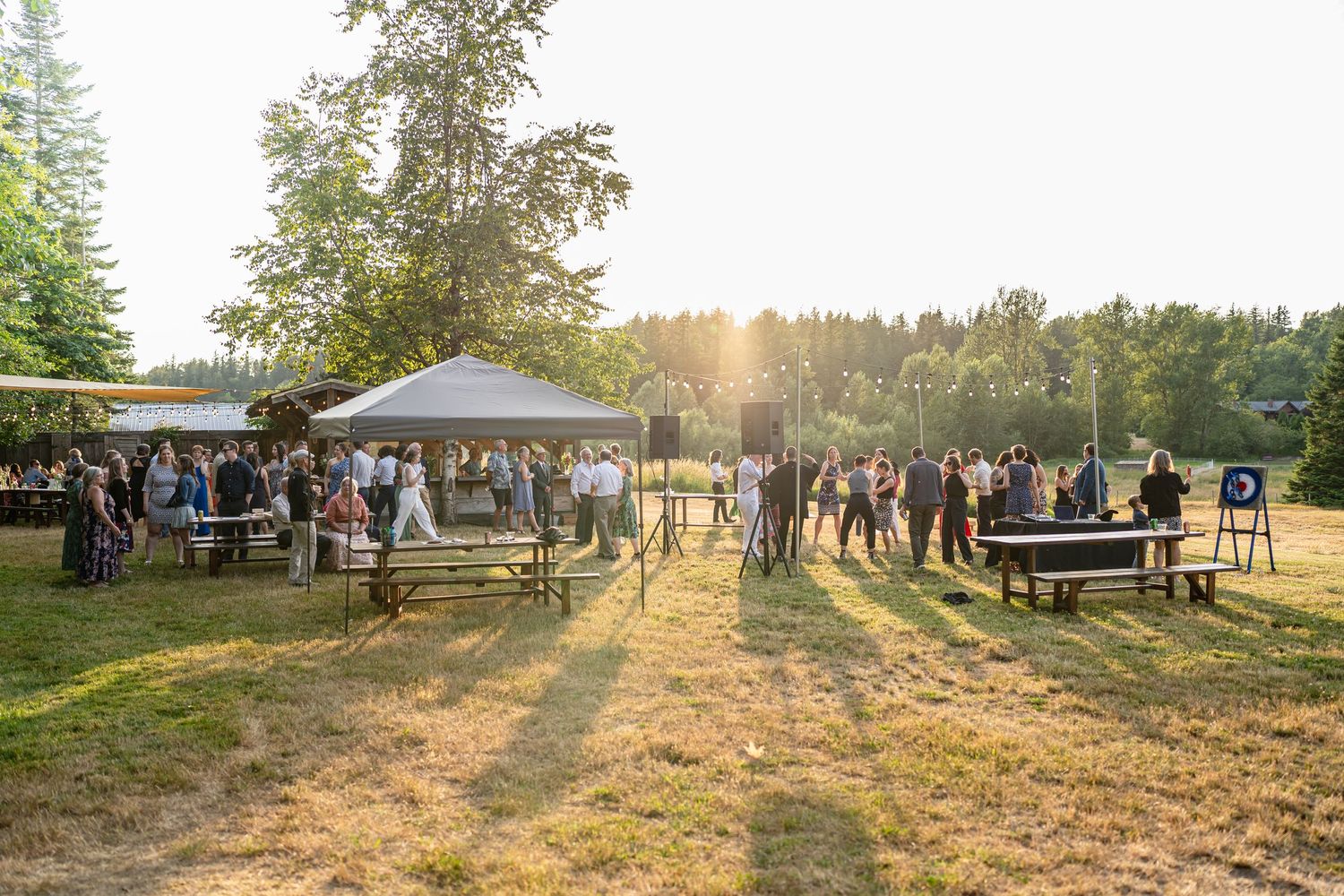 Sunset wedding reception with guests mingling under white tents in a grassy field.
