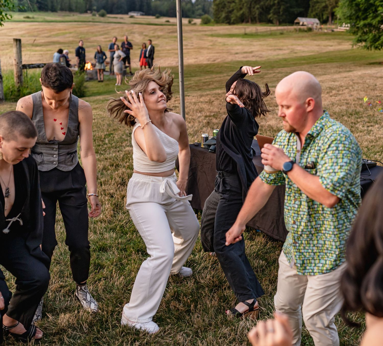 Group of wedding guests dancing energetically on grass field.