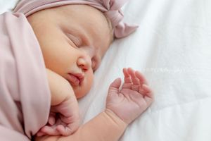 Sleeping baby in pink clothing on white bedding.