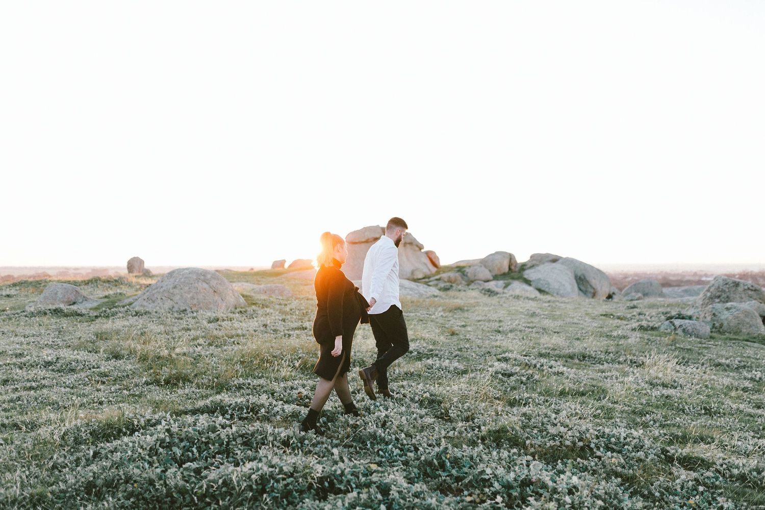 Two people share a romantic moment on a rocky outcrop during golden hour.