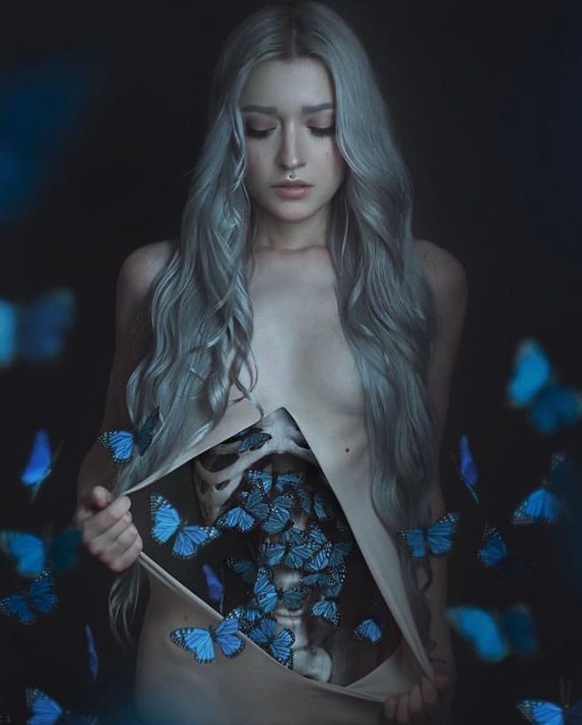 Ethereal portrait with blue butterflies emerging from a person's torso against a dark background.